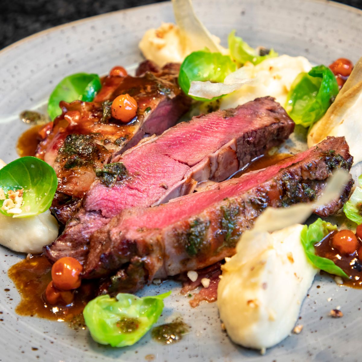 A plate of sliced venison meat with mashed potatoes and fresh herbs.