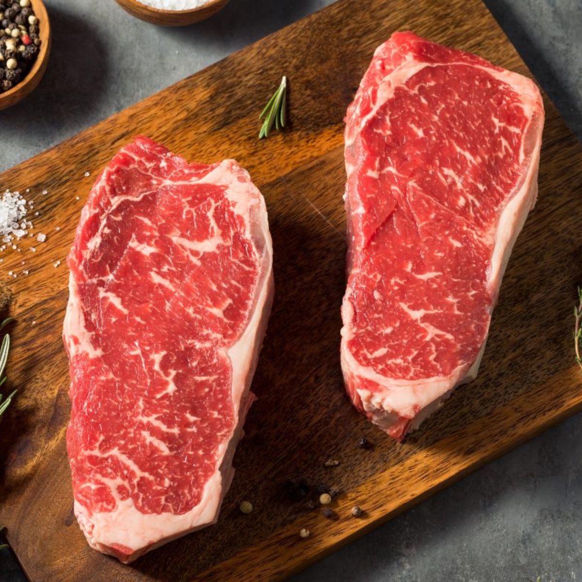 Two New York strip steak cuts on a wood cutting board