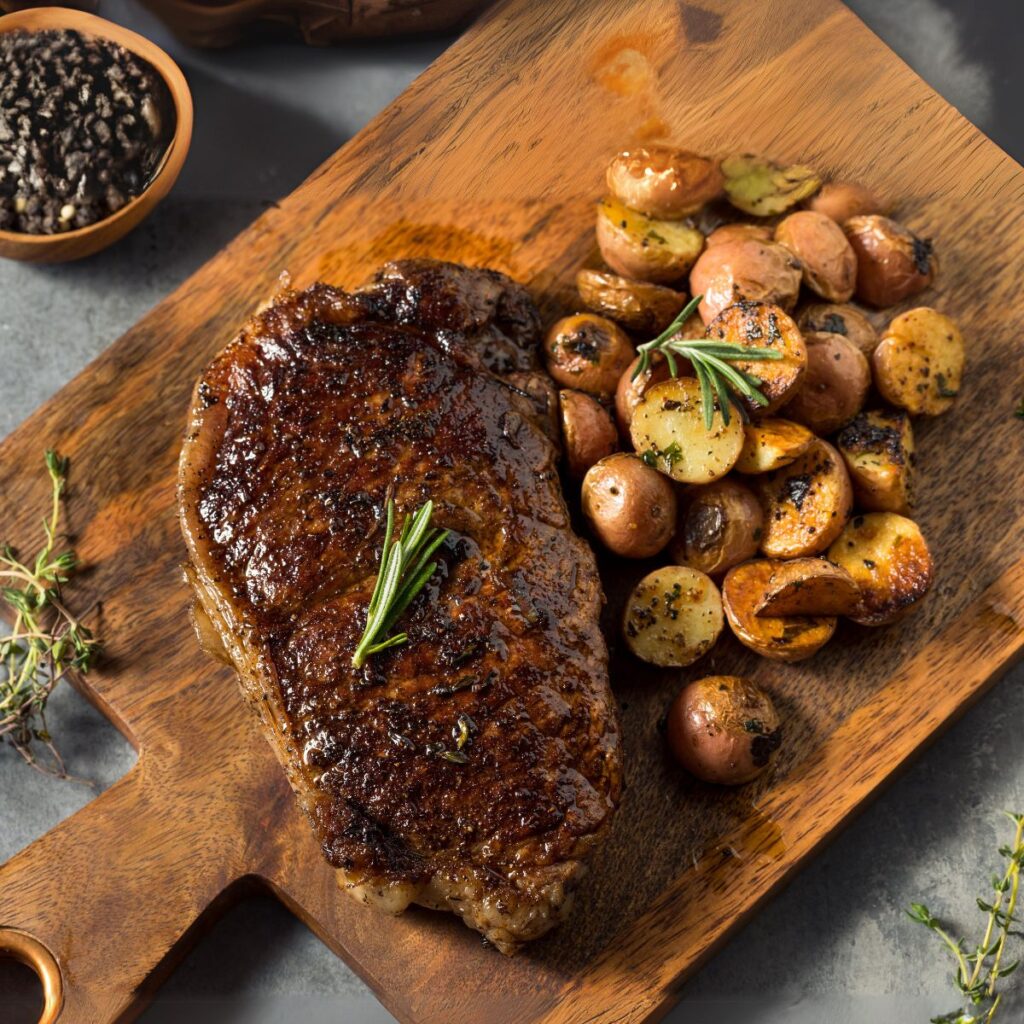 A beautifully cooked New York strip steak with roasted potatoes on the side, all placed in a cutting board.