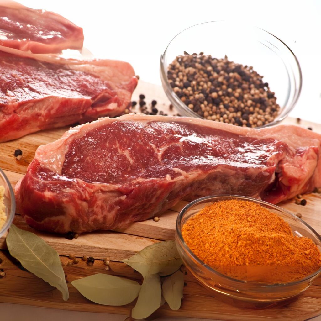 New York strip steak cuts on a wood cutting board surrounded with spices.